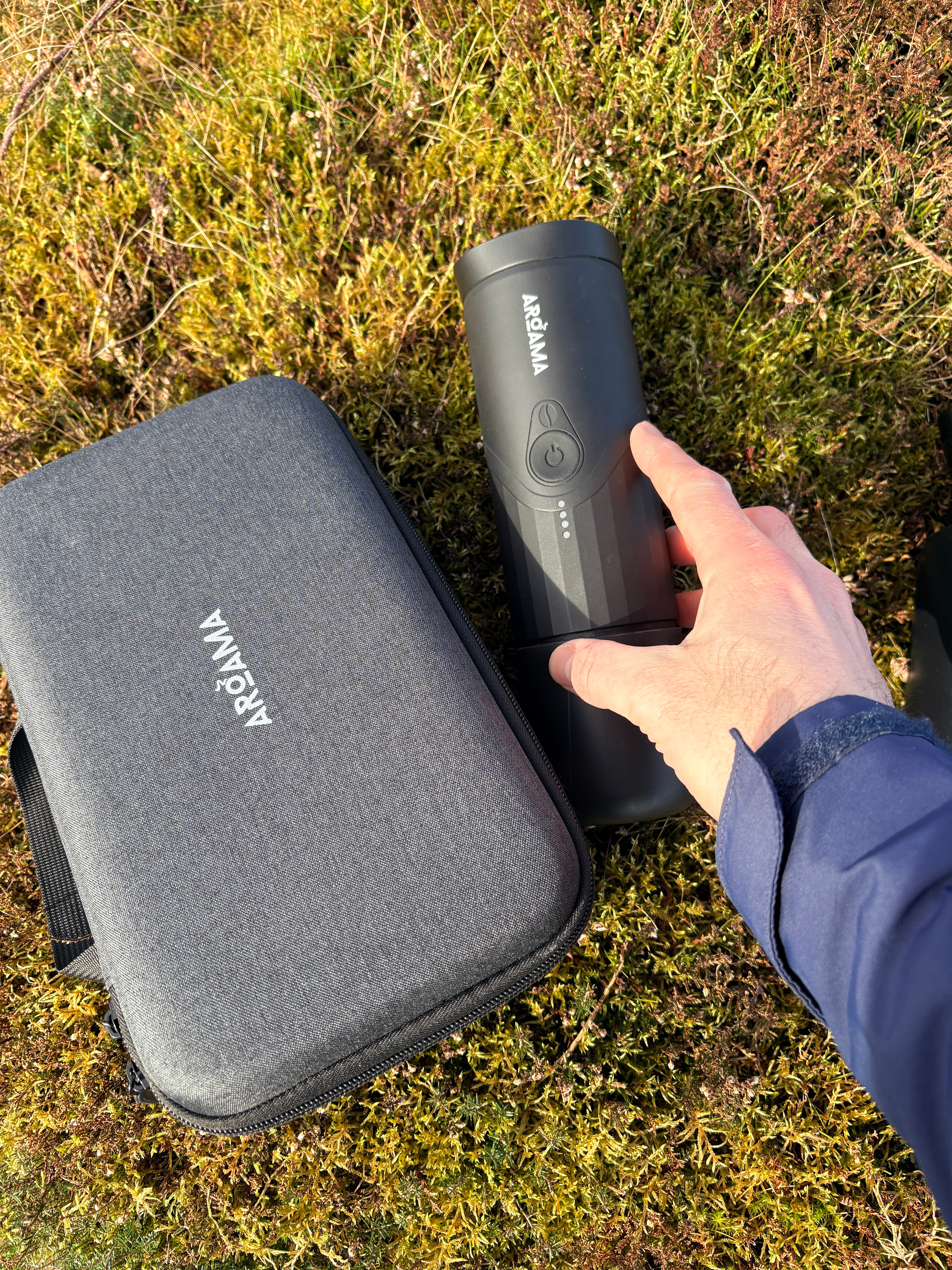 Person holding a portable coffee maker to its case on grass