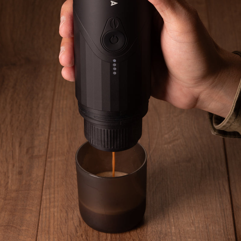 Hand holding a black Aroma coffee maker on a wooden surface