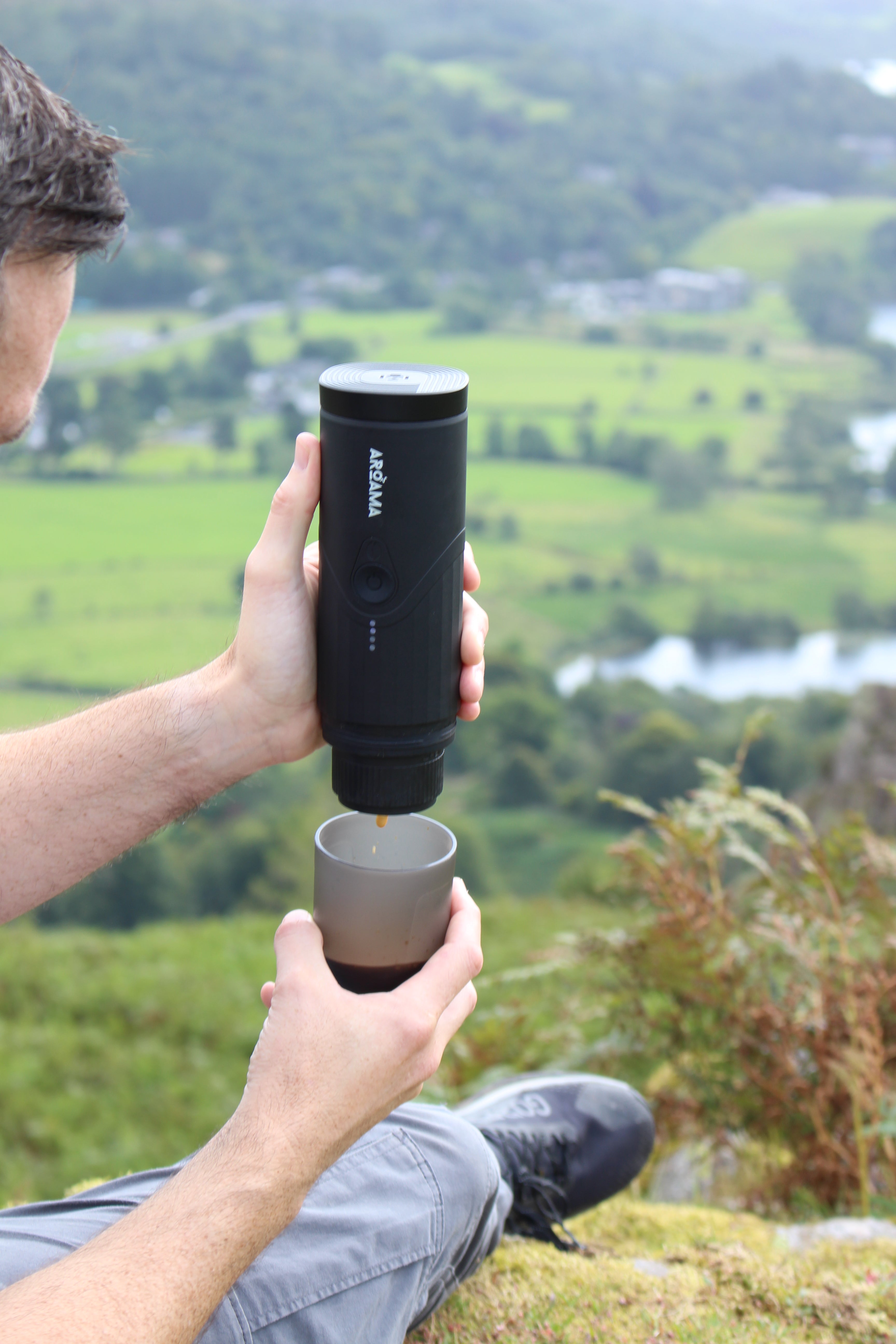 Person holding a black and gray Aroma coffee maker against a natural background